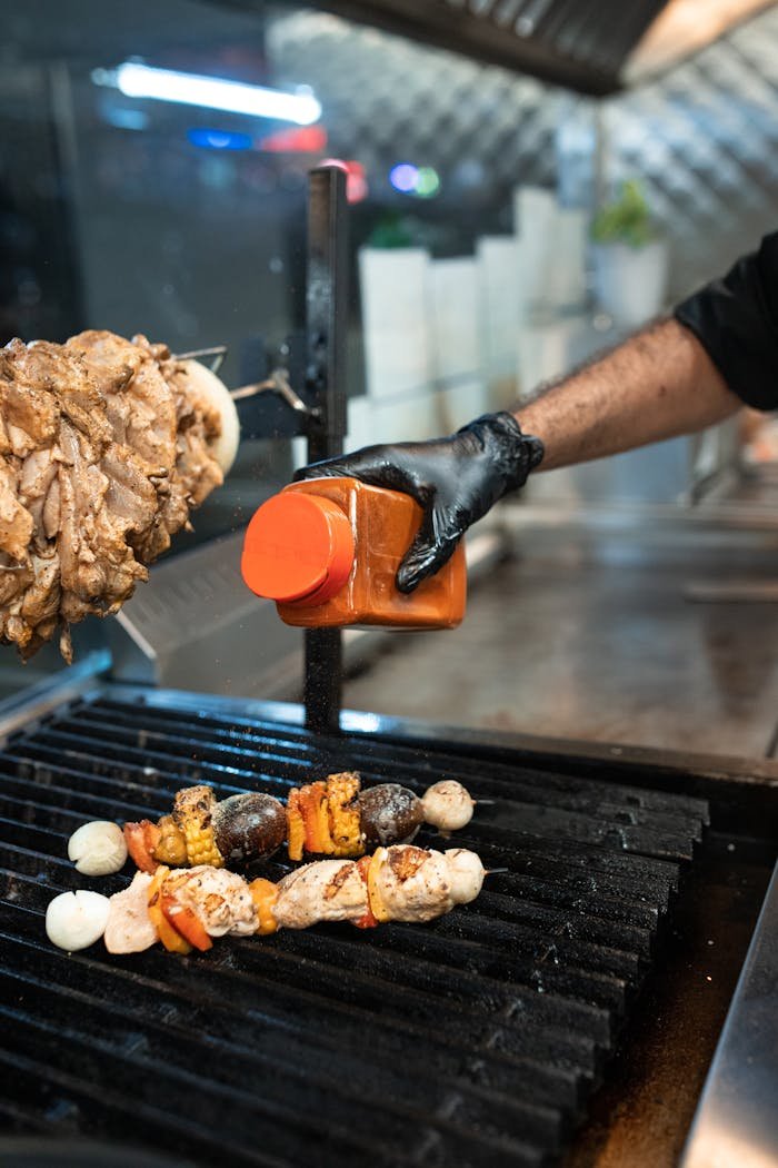 A chef seasons skewers on a grill, enhancing flavors in a restaurant kitchen setting.